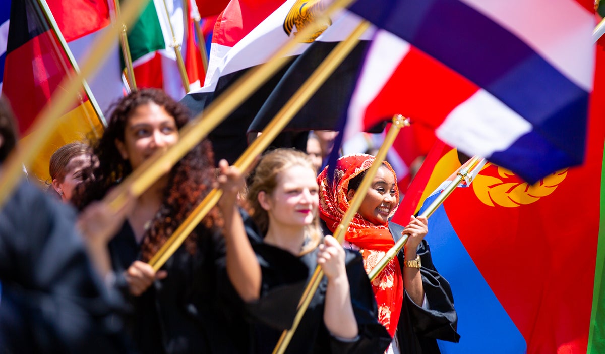 Close up photo of a parade of students holding flags from a variety of countries around the world.