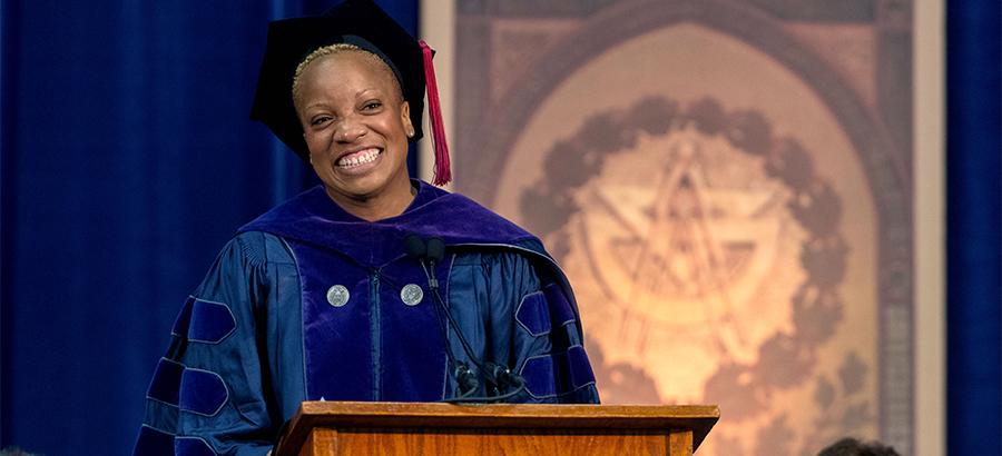 Pam Nwaoko, a black woman wearing academic regalia, speaks from the commencement podium.