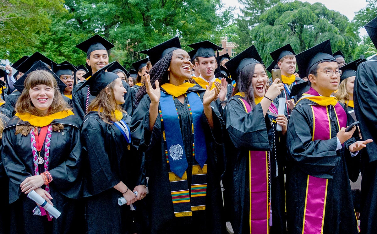 A group of graduates in academic regalia celebrate outside.