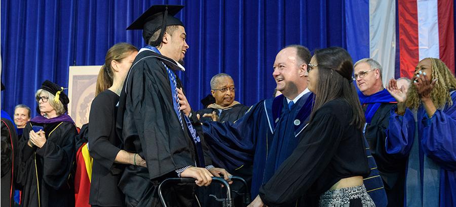 President DeGioia congratulates a graduate on a stage, surrounded by other faculty members in academic regalia.