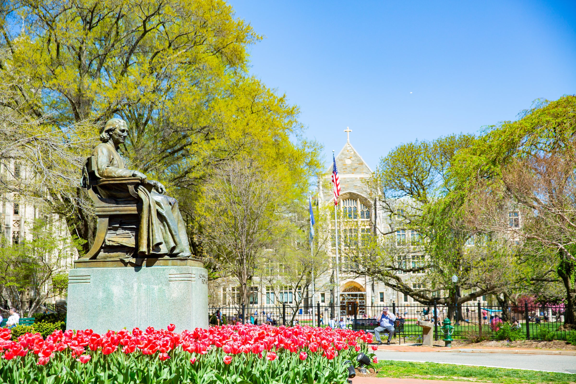 The John Carroll statue surrounded by flowers, with White-Gravenor Hall in the background