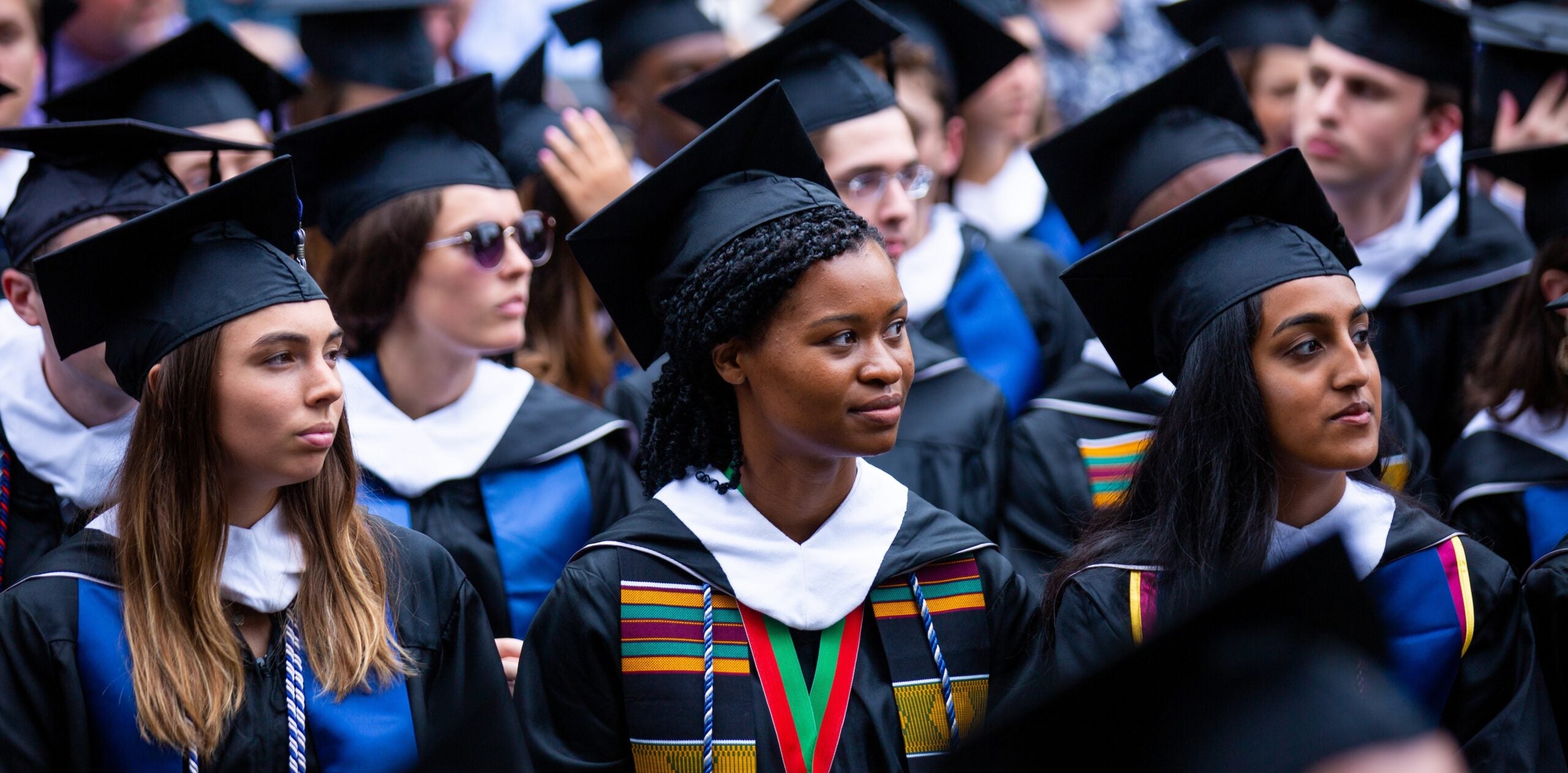 A group of graduates in caps and gowns, sitting at a commencement ceremony