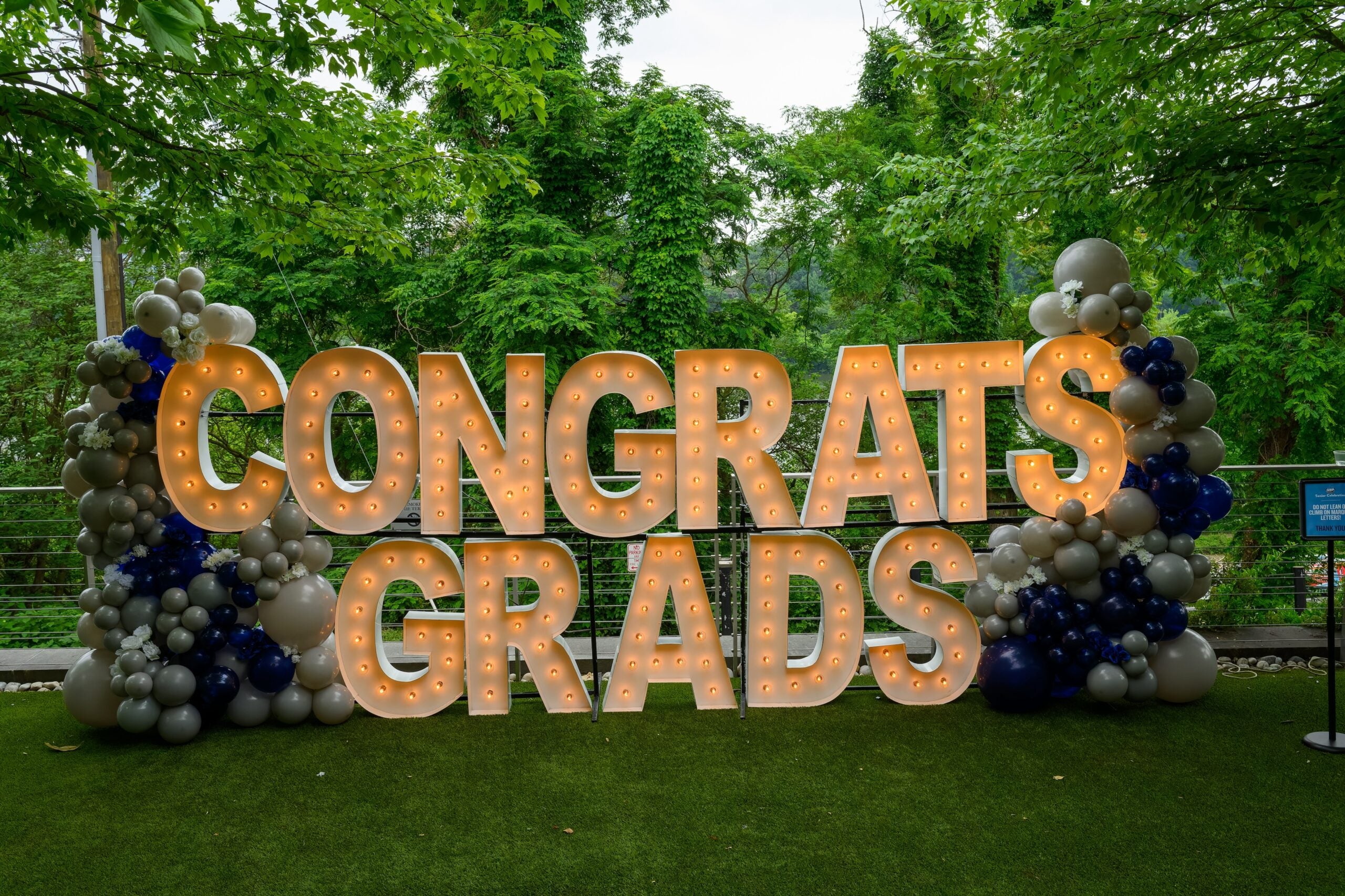 Lighted outdoor sign saying Congrats Grads, surrounded by balloons