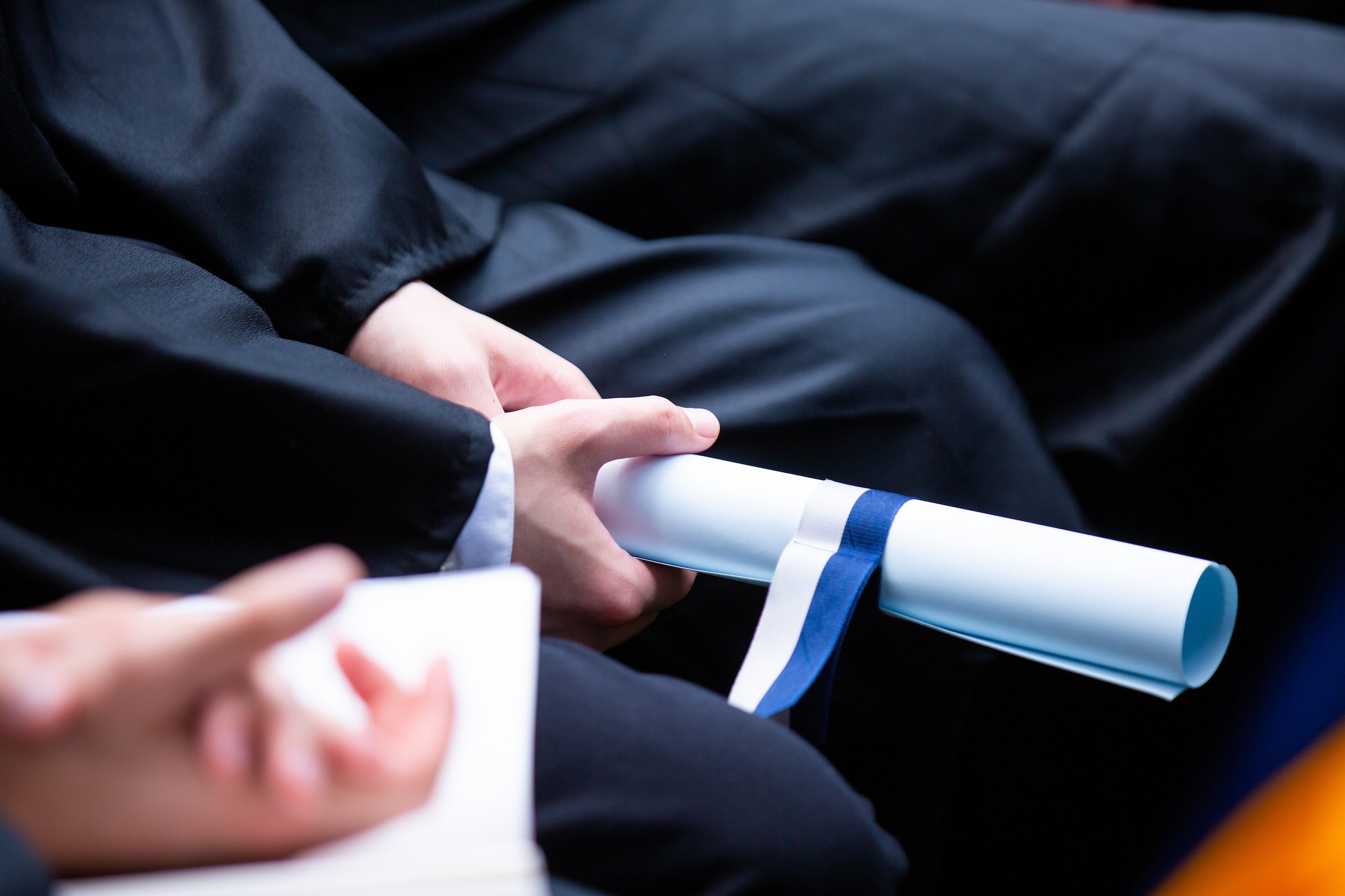 A graduate holds a rolled-up diploma in their lap.
